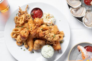Fisherman's platter consisting of colossal naked shrimp, sea scallops, local whitefish and calamari on white plate.