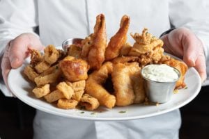 Chef holding fisherman's platter including colossal naked shrimp, sea scallops, local whitefish and calamari.